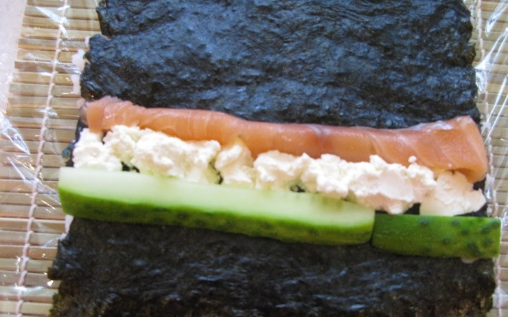 1. Этап. Ролл с лососем: 4. На перевернутый лист выкладываем сыр, огурец и лосось, плотно заворачиваем ролл, после этого выкладываем поверх икру и опять заворачиваем с помощью коврика, чтобы икра равномерно распределилась.