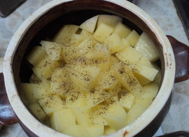 1. Этап. Жаркое в горшочке в духовке: Горшочек смазываем небольшим количеством растительного масла и выкладываем в него сначала лук, затем мясо и картофель. Сверху посыпаем солью и черным молотым перцем, а при желании можете добавить и другие специи.