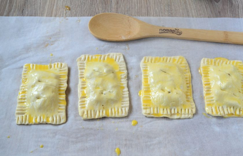 1. Этап. Кармашки с яблочными пирожками: Края смажьте взбитым яйцом, накройте сверху прямоугольниками теста, вилкой закрепите края. Благодаря тому, что мы смазывали края яйцом, тесто хорошо сцепится. Сверху пирожки также смажьте взбитым яйцом, сделайте небольшие надрезы. Переложите пирожки на противень, застеленный пергаментом, и запекайте в духовке 20-25 минут при температуре 180 градусов. Запекать нужно до золотистого цвета.