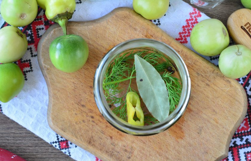 1. Этап. Зеленые помидоры со свеклой на зиму: На дно чистых банок выложите специи — укроп, кусочек горького перца, лавровый лист и перец горошком.