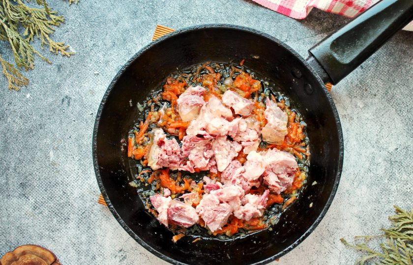 1. Этап. Кукурузная каша с тушенкой: Тушенку порежьте на кусочки и добавьте в сковороду с овощами.