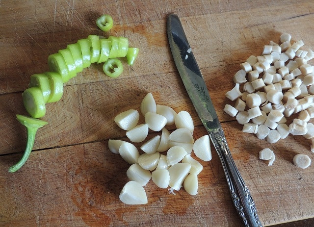 1. Этап. Маленькие огурчики на зиму: Порежьте зубчики чеснока на дольки, корень хрена и перец порежьте колечками. Банки помойте (стерилизовать их необязательно).