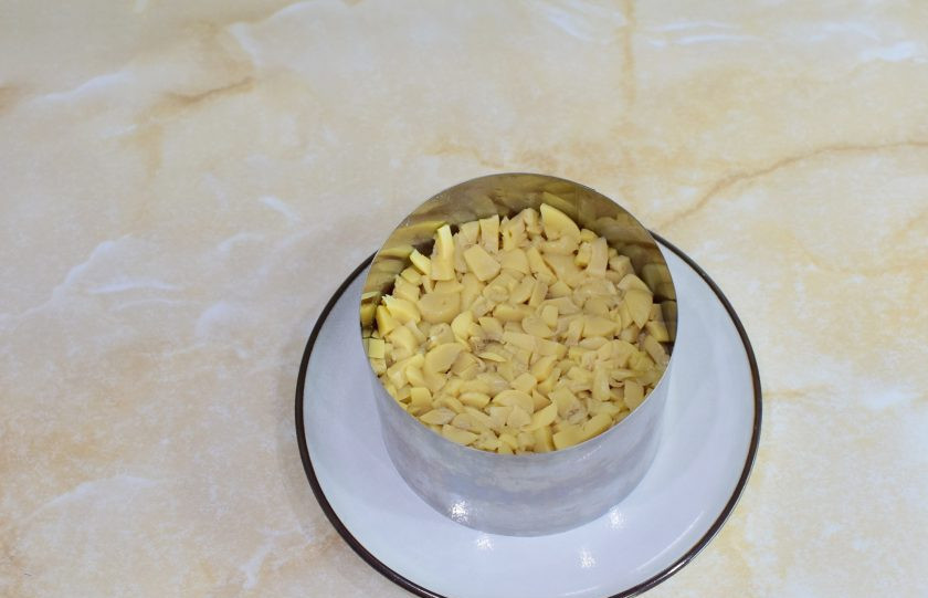 1. Этап. Салат с курицей, сыром и маринованными грибами: С маринованных грибов слейте жидкость. Грибы мелко нарежьте и выложите в форму следующим слоем. Смажьте майонезом.