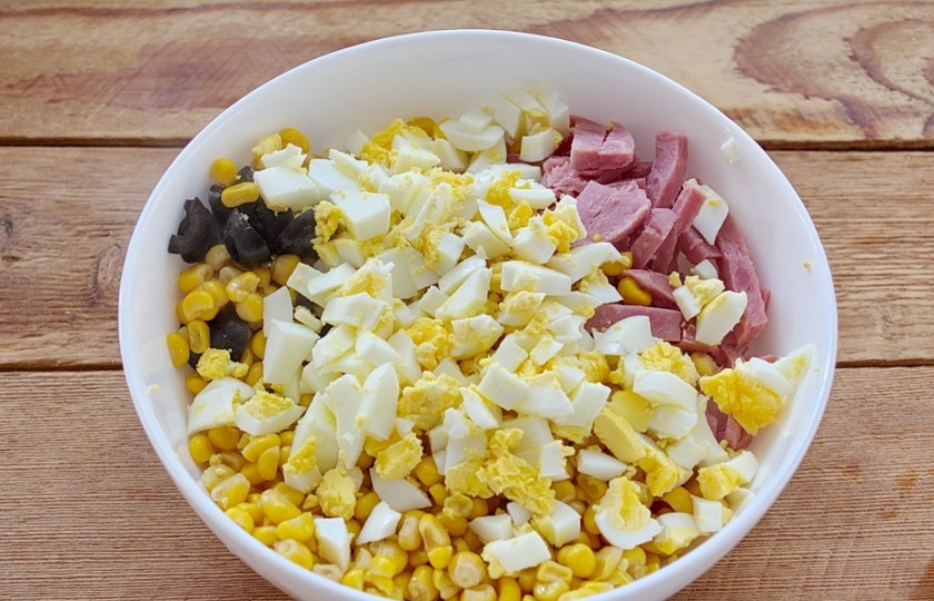 1. Этап. Салат с ветчиной Пятерка: В салатнике соедините ветчину, грибы, маслины, отварные куриные яйца и добавьте кукурузу консервированную.