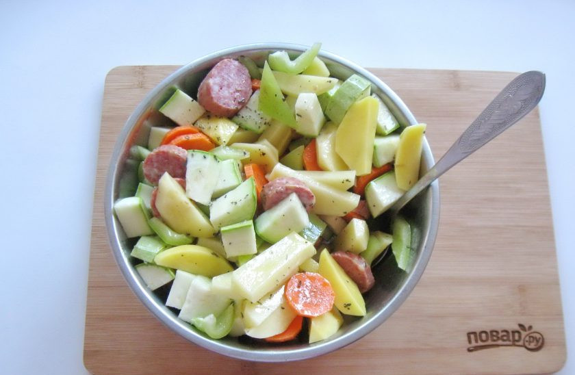 1. Этап. Картофель с колбасками в духовке: Влейте оливковое масло с приправой в смесь овощей с колбасками, посолите и перемешайте.