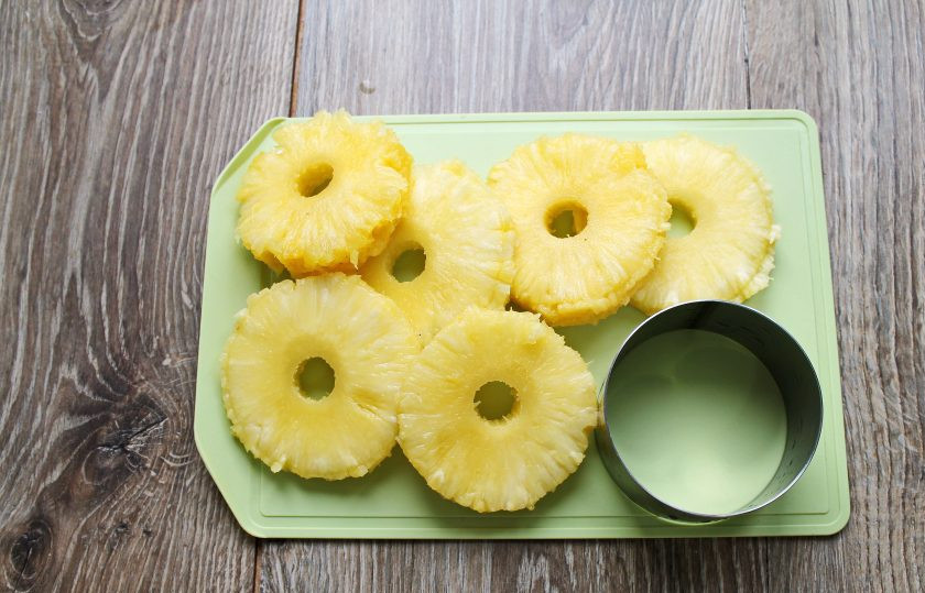 1. Этап. Ананасы в сиропе на зиму: Отрежьте верхушку ананаса, срежьте все корки, удалите оставшиеся вкрапления. Порежьте ананас на кружочки толщиной 0.5-1 сантиметр. Вырежьте твердую серединку, края подравняйте при помощи кухонного кольца.