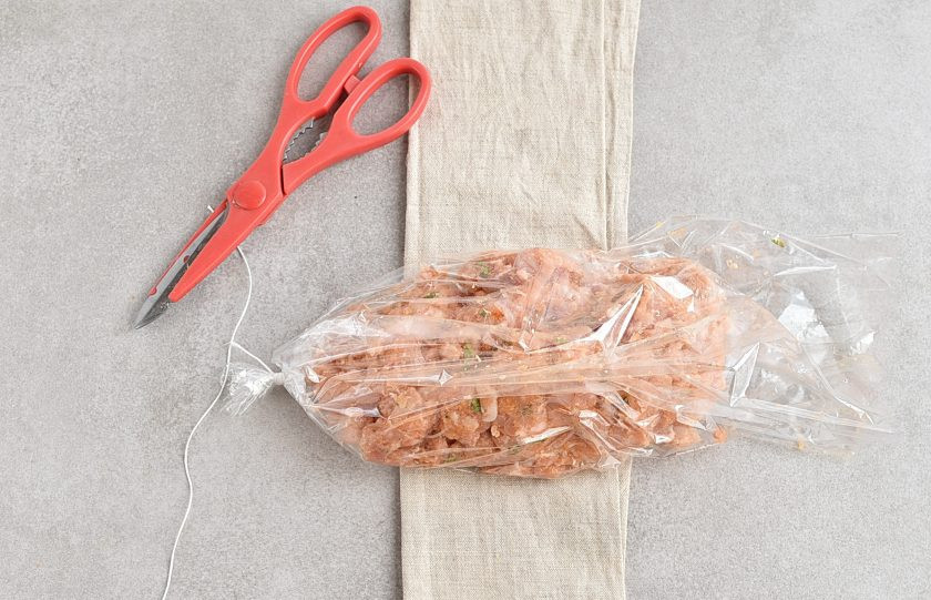 1. Этап. Домашняя ветчина из курицы: Отрежьте кусок рукава для запекания нужной длинны и крепко завяжите один конец. Выложите фарш в рукав, располагая его по одному длинному краю.