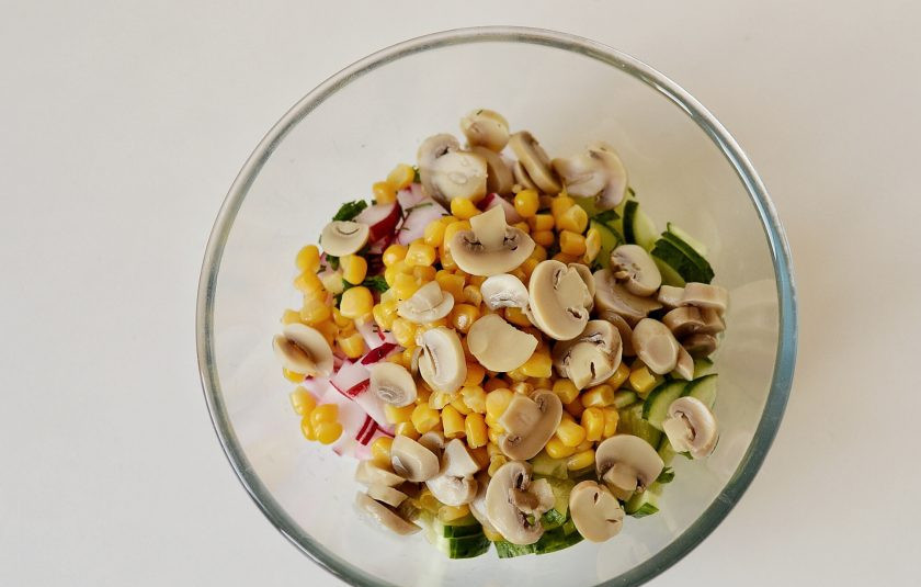 1. Этап. Салат с кукурузой, грибами и огурцами: Добавьте кукурузу и консервированные шампиньоны.