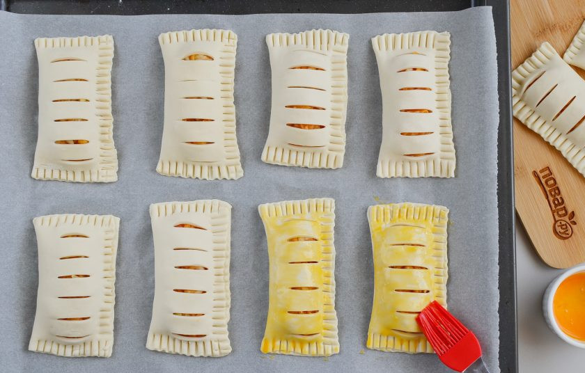 1. Этап. Тыква в слоеном тесте: Противни застелите пергаментом. Духовку прогрейте до 200-220 градусов. Выложите слойки на противни, смажьте желтком. Для 20 слоек нужно два желтка или один крупный, немного разбавленный водой или молоком.