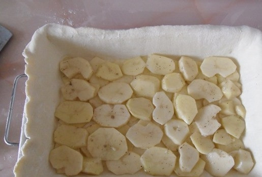 1. Этап. Пирог с мясом из слоеного дрожжевого теста: Картофель очистите и нарежьте кружочками. Получившиеся кругляши выложите на растеленный кусок теста. Поперчите и посолите сверху картошку.