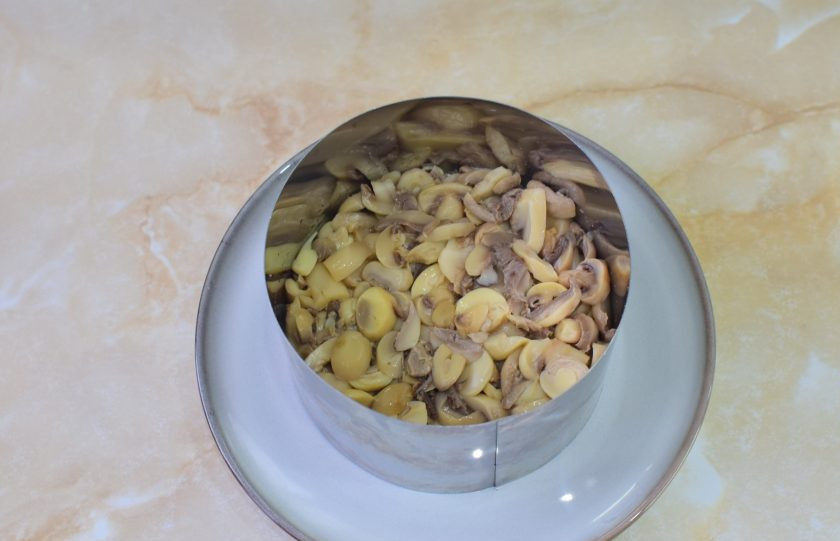 1. Этап. Салат Дубок с курицей и шампиньонами: Вторым слоем выложите консервированные шампиньоны, нарезанные на кусочки.