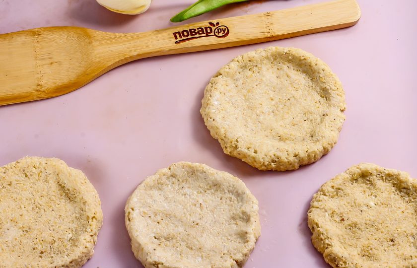 1. Этап. Полезные ватрушки с творогом: Смажьте противень или бумагу для выпекания сливочным маслом. Разделите овсяное тесто на равные части и каждую из них скатайте в руках в колобок. Руки смочите в воде для этого. Расплющьте каждый колобок теста на противне и сформируйте лепешки с бортиками.