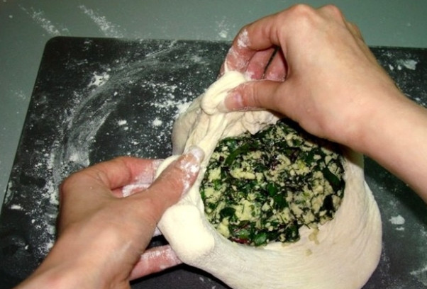 1. Этап. Осетинский пирог со свекольной ботвой: 5. Присыпьте поверхность для приготовления мукой. Руки смочите растительным жиром. Третью часть теста сформируйте в виде лепешки. Положите в центр третью часть начинки. Подогните края теста и сформируйте большой шар.