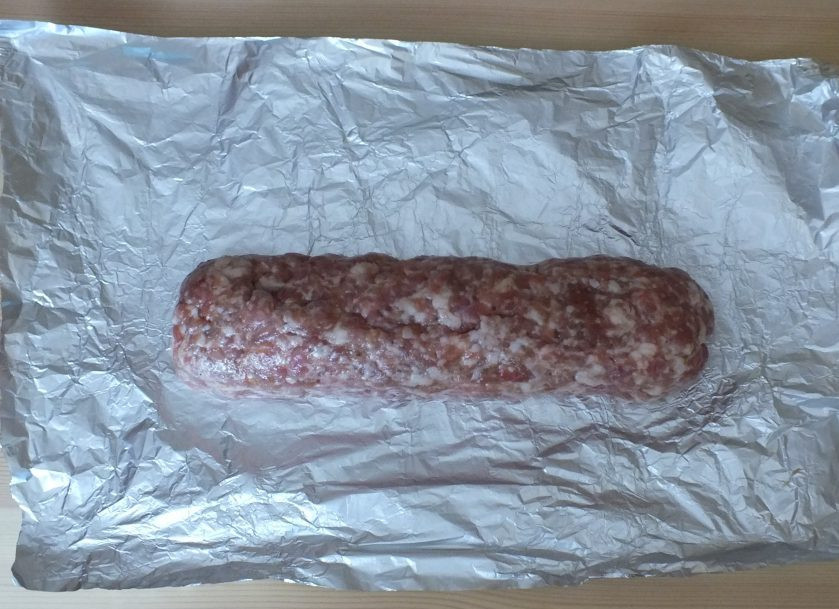 1. Этап. Домашняя колбаса в фольге: По истечении времени, достаньте фарш из холодильника, еще раз хорошо перемешайте. Оторвите 2 листа фольги (ориентировочно 45*25 см. каждый). Фарш поделите на две части. Выложите одну часть на лист фольги. Придайте форму брусочка. Повторите процесс со второй частью фарша.