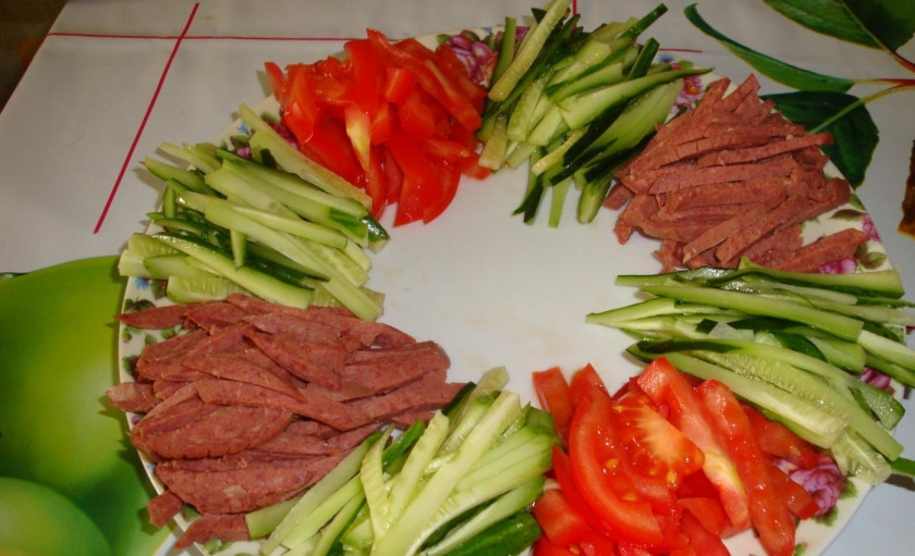 1. Этап. Салат Радуга: Тонкой соломкой режем огурцы, укладываем их между колбасой и томатами.