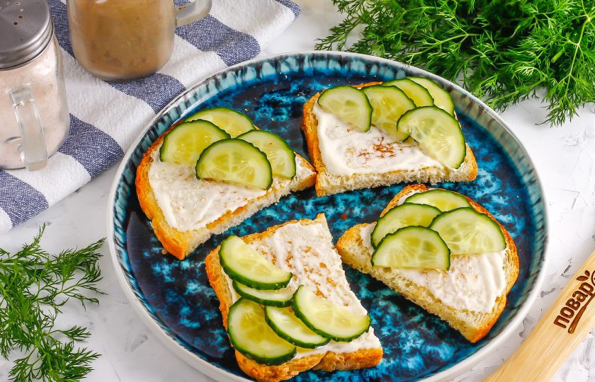 1. Этап. Брускетты с печенью трески: Промойте огурец в воде, срежьте хвостики и разрежьте пополам вертикально. Нарежьте одну половину овоща полукольцами и выложите их на половинки брускетт.