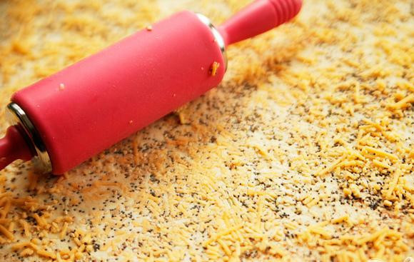 1. Этап. Пряные сырные палочки: 4. Посыпать сверху мелко тертым сыром Чеддер. С помощью скалки вдавить сыр в тесто.