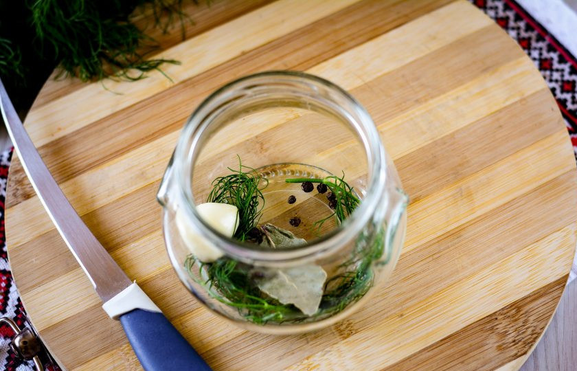 1. Этап. Салат из переросших огурцов на зиму без стерилизации: На дно подготовленной стерилизованной банки выложите все специи: чеснок, укроп, перец горошком и лавровый лист.