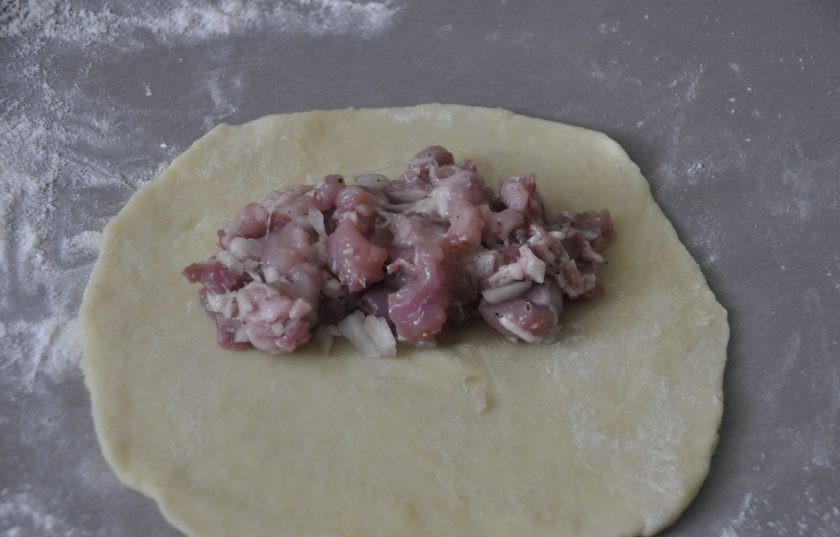 1. Этап. Кибинай: Присыпьте стол мукой, раскатайте тесто в лепешку, на один край лепешки выложите мясную начинку.