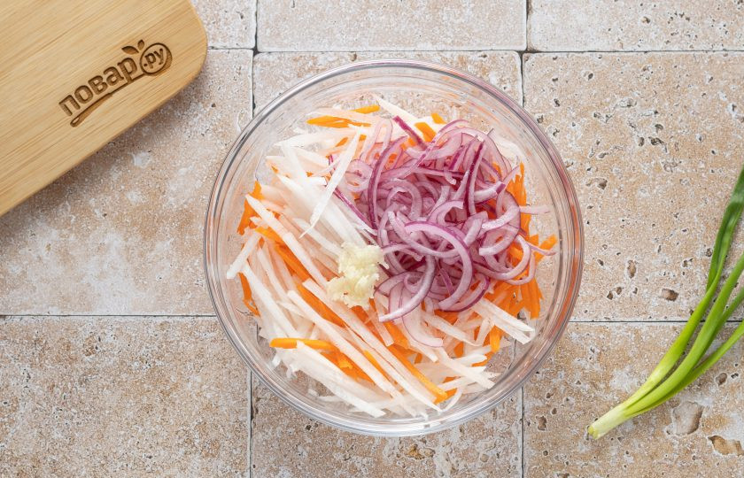 1. Этап. Салат из дайкона по-корейски: Соедините подготовленные овощи в глубокой миске. Добавьте измельченный зубчик чеснока.