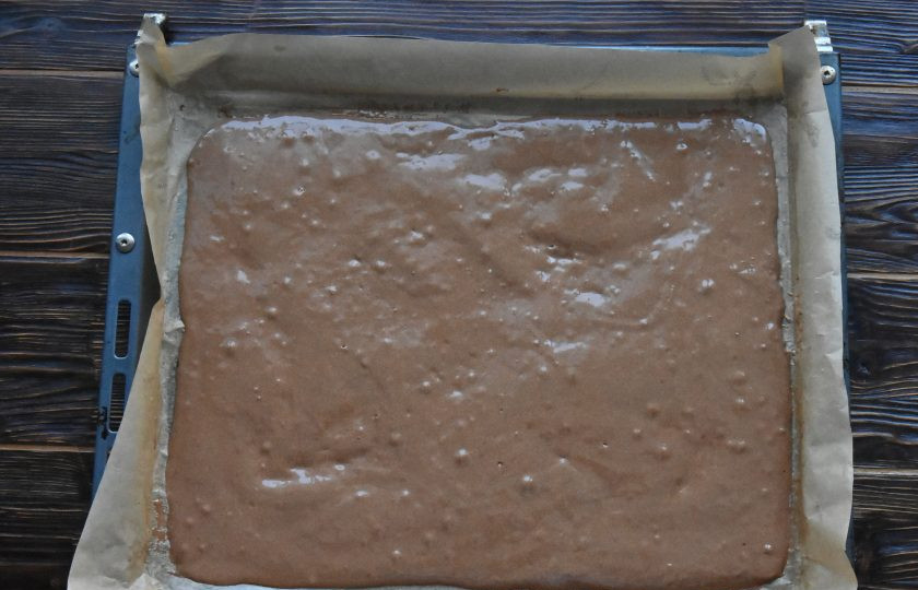 1. Этап. Торт Рождественское полено: Противень выстелите пергаментной бумагой и выложите подготовленное тесто. Разровняйте тесто по всей поверхности ровным слоем.