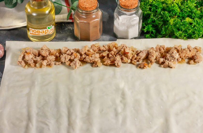 1. Этап. Пирог с мясом из теста Фило: Отделите два листа теста. Смажьте один лист растительным маслом и выложите на него другой. На широкий край листа выложите треть мясной начинки и скрутите рулетиком. Так поступите и с остальными листами теста и начинкой.