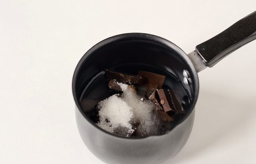 1. Этап. Постный шоколадный мусс: Сверху налейте воду, добавьте сахар и вкусовой акцент, я использую финиковый сироп. Поставьте ковшик на средний огонь. Помешивайте лопаткой до полного растворения шоколада.