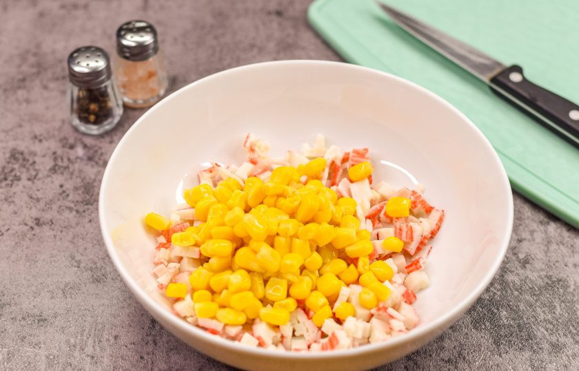 1. Этап. Закуска на чипсах на праздничный стол: Откройте консервированную кукурузу и слейте сок. Переложите кукурузу в миску к палочкам.