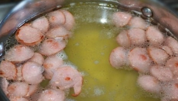 1. Этап. Солянка из сосисок: Кипятим в большой кастрюле воду. Кладем туда же очищенный и порезанный картофель. Тем временем нарезаем колечками несколько сосисок, быстро обжариваем их на сковороде и отправляем к картофелю.