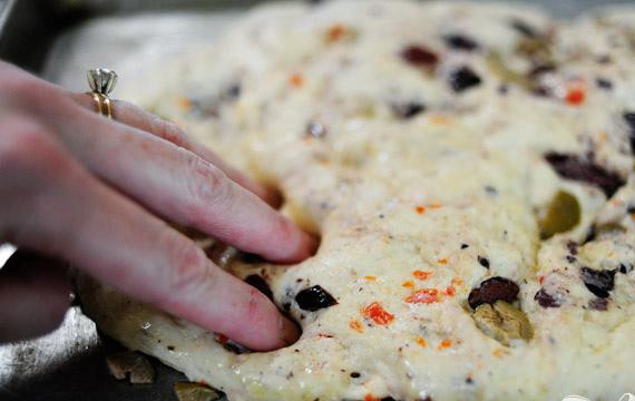 1. Этап. Фокачча с маслинами: 6. Разогреть духовку до 200 градусов. Удалит пленку и подушечками пальцев сделать углублениями по всей поверхности теста. Полить поверхность оливковым маслом и посыпать солью.