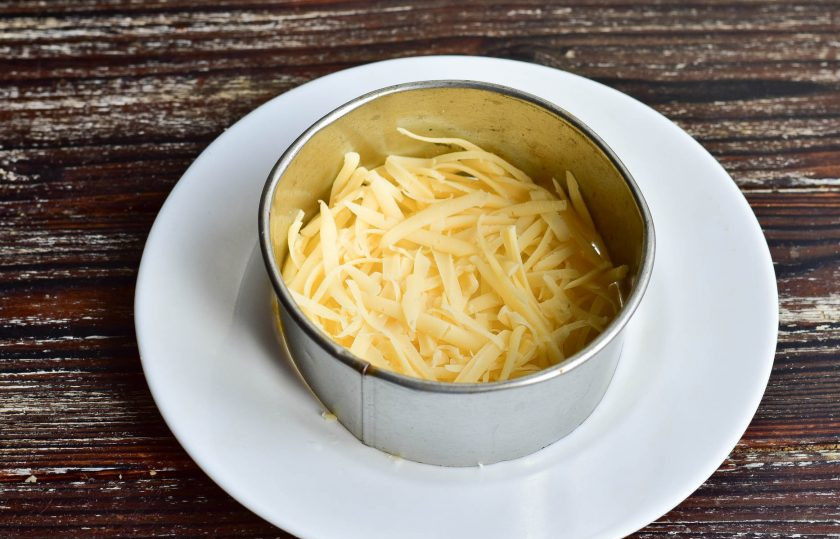 1. Этап. Салат Чебурашка с курицей: На плоское блюдо установите формировочный круг. Выложите первым слоем тертый на крупной терке твердый сыр.