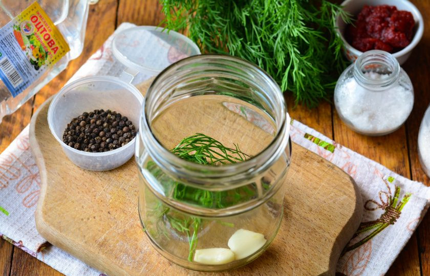 1. Этап. Огурцы в томатной пасте на зиму: Сложите на дно простерилизованной банки специи: укроп, чеснок и перец горошком.