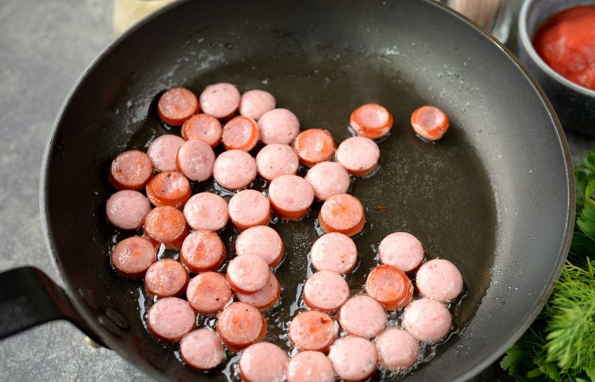 1. Этап. Американский обед: Налейте растительное масло в сковороду, выложите в него нарезанные кружочками колбаски, обжарьте в течение минуты на умеренном огне.