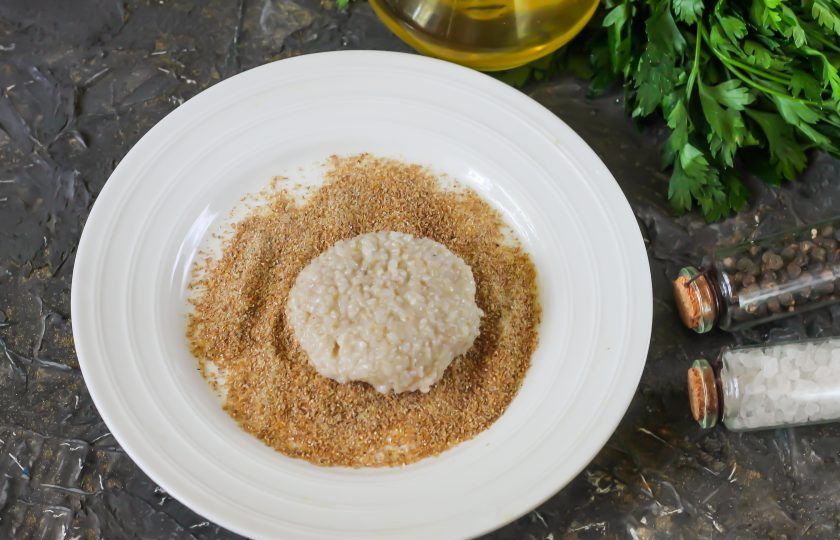 1. Этап. Котлеты из пшеничной каши: Высыпьте панировочные сухари на тарелку, смочите ладони в холодной воде и скатайте из части пшеничной массы заготовку котлеты, обпанируйте ее в сухарях с обеих сторон.