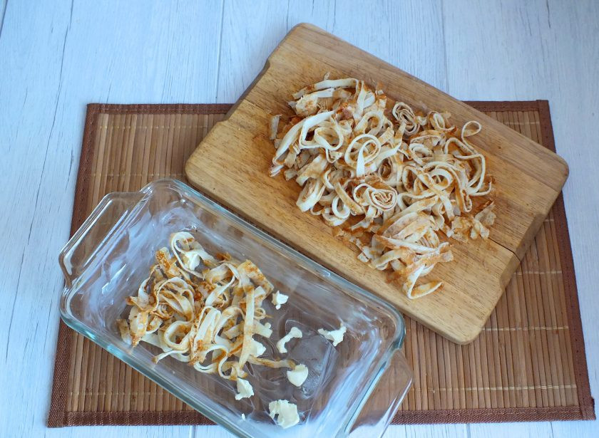 1. Этап. Лапшевник из блинов: Возьмите глубокую форму, смажьте маслом, остатки раскрошите на дне. Выложите блинную лапшу, равномерно распределяя.