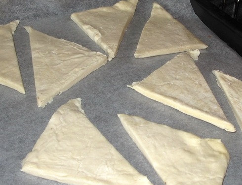 1. Этап. Курица по-королевски: Слоеное тесто, не раскатывая, разрезаем на 4 квадрата, а те в свою очередь режем по диагонали. Таким образом, у нас должно получиться 8 треугольников слоеного теста. Противень устилаем пергаментной бумагой и выкладываем на него наши треугольники, смазываем их взбитым яйцом. Ставим в разогретую до 200 градусов духовку на пол часа.