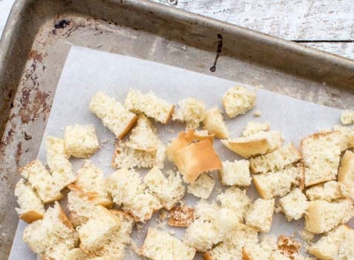 1. Этап. Хрустящие сухарики: 2. Нагрейте духовку до 170 градусов, выложите кубики хлеба на противень, застеленный пергаментной бумагой, распылите растительное масло на хлеб.