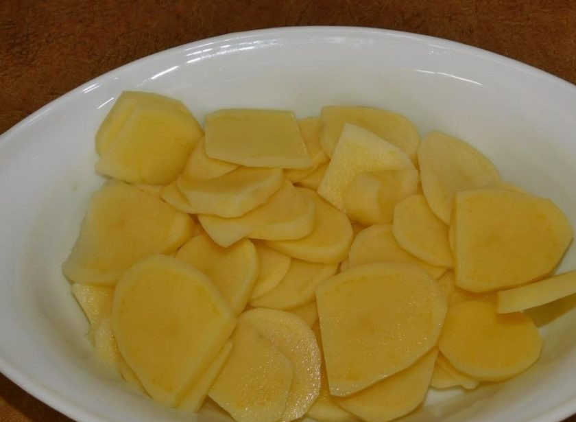 1. Этап. Картофель с грибами и сыром в духовке: Картофель почистите и нарежьте кружками. Выложите в форму для запекания, смазанную маслом. Немного посолите.
