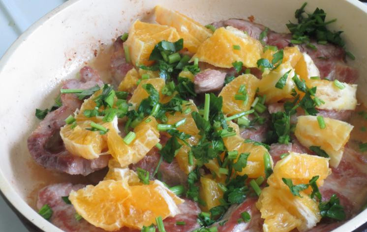 1. Этап. Свиная шейка на сковороде: Затем с апельсина снимаем корку и нарезаем его маленькими кусочками, зелень рубим. Мясо солим, перчим, перемешиваем. Сверху кладем апельсины и зелень.