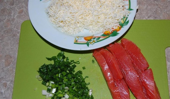1. Этап. Блины с семгой и сыром: Нарезаем рыбу тонкими пластиками, сыр натираем на мелкой терке, а зеленый лук мелко нарезаем. Вместо плавленых сырков можно взять любой другой сыр, но к нему нужно будет добавить немного майонеза, чтобы получилась слегка клейкая масса. В этом случае сыр не будет высыпаться из блина.