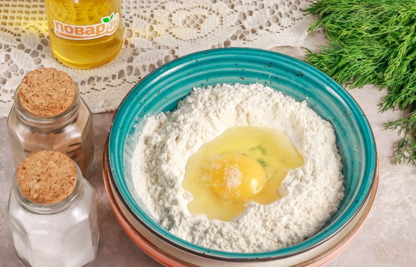 1. Этап. Пельмени с рыбой По-сахалински: Всыпьте муку в глубокую емкость и сделайте в ней углубление. Всыпьте в него 2 щепотки соли и вбейте куриное яйцо. Влейте воду и замесите тесто.