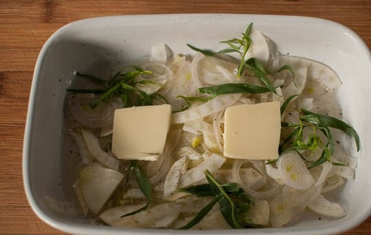 1. Этап. Семга в фольге в духовке: В форму для запекания выложите тонко порезанный лук, фенхель, листочки эстрагона, добавьте вино и пару кусочков масла. Посолите немного.