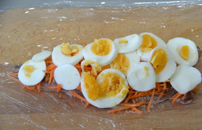 1. Этап. Скумбрия по-царски: Застелите разделочную доску двойным слоем пищевой плёнки, выложите на пленку филе скумбрии кожицей вниз, чуть-чуть подсолите и посыпьте специями для рыбы, посыпьте желатином, выложите морковь, яйца.