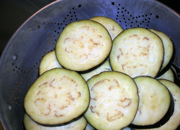 1. Этап. Баклажаны с сыром и чесноком: 2. Посолите кружочки бакажана солью и выложите в дуршлаг. Сверху прижмите тарелочкой и грузом (банкой с водой) и оставьте на час.