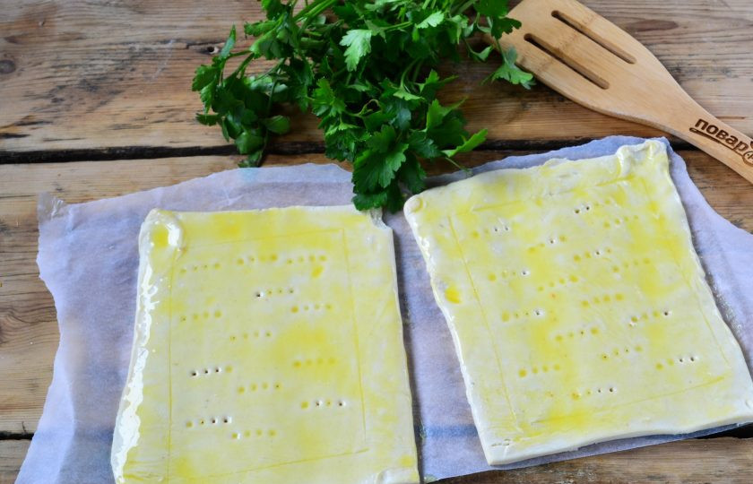 1. Этап. Пикантный слоеный пирог с беконом и глазуньей: Тесто раскатайте и разрежьте на 2 прямоугольника. Сделайте легкий надрез в виде квадрата, а в его середине сделайте несколько проколов вилкой. Смажьте куски теста желтком и отправьте в духовку, разогретую до 190 градусов, на 10 минут.