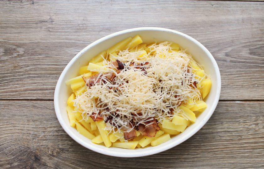 1. Этап. Картофель с беконом в сметанной заливке: Добавьте к картофелю с беконом 2/3 натертого сыра и перемешайте.