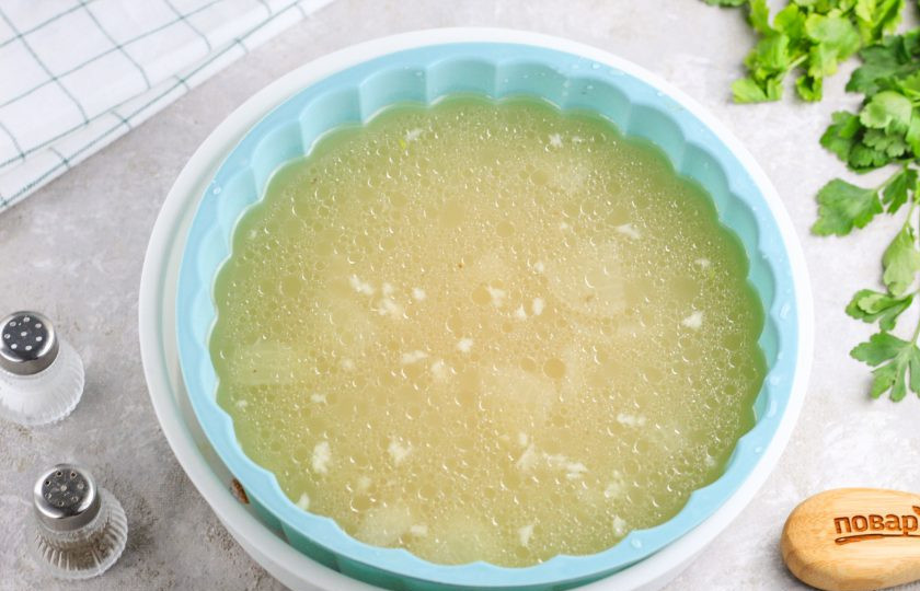 1. Этап. Желе из мясного бульона: Ножки извлеките из бульона, а его перелейте в силиконовую форму или в емкость с высокими бортиками.