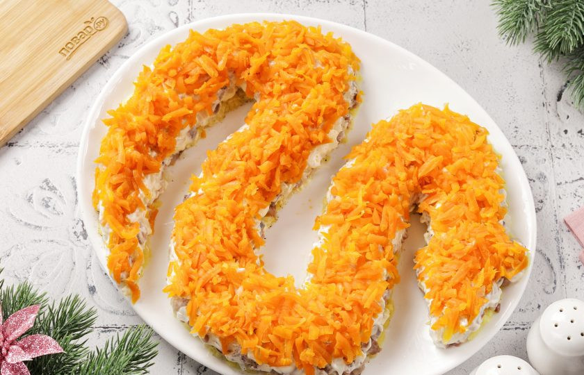 1. Этап. Селедка под шубой на год Змеи 2025: На лук выложите тертую на крупной терке морковь. Посолите и смажьте майонезом.