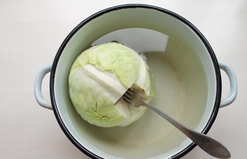1. Этап. Листья капусты для голубцов на зиму: Удалите у капусты верхние и поврежденные листья. Вырежьте под угол кочерыжку и вставьте вилку. В глубокую кастрюлю налейте воду и доведите до кипения на среднем огне. Опустите в нее капусту и варите в течение 5-6 минут. Достаньте капусту и снимите листья, которые стали мягкими. Верните капусту обратно, варите и снимайте листья, пока не останется маленький кочан.
