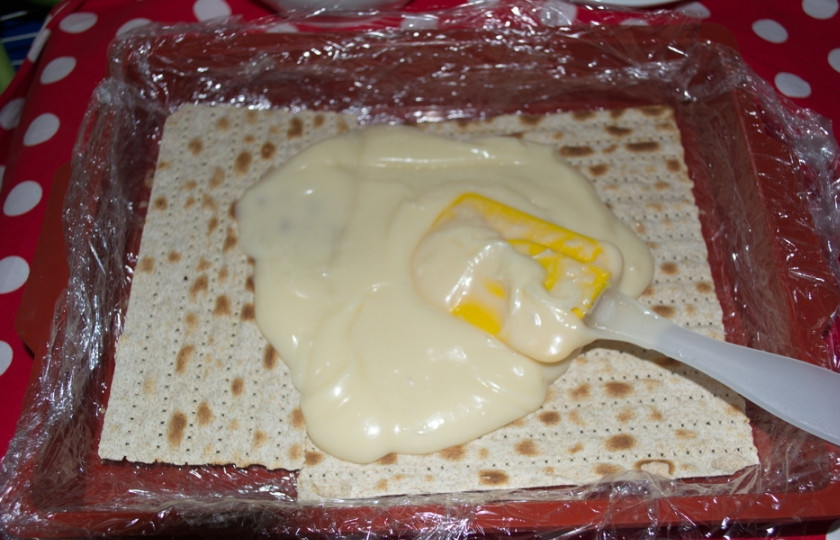 1. Этап. Наполеон из мацы: В остывший крем налейте оставшееся молоко. Взбейте. Крем станет более жидким. Добавьте масло комнатной температуры в крем, и тщательно все размешайте. В форму уложите несколько листиков мацы в один слой. Сверху на мацу выложите 3 ст. ложки крема. Распределите по всей поверхности мацы. Накройте новыми листиками мацы.